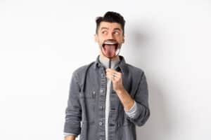 homem jovem mostrando a lingua com uma lupa olhando para a esquerda em pe sobre um fundo branco