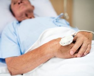 paciente idoso deitado em uma cama de hospital, com um monitor de pulso preso à mão, representando o cuidado contínuo necessário para tratar condições crônicas que podem incluir ferida que não cicatriza.