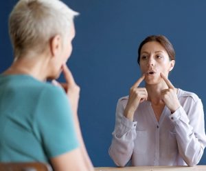 mulher em um consultório tratando o sulco vocal participando de uma sessão de fonoterapia. Ela parece estar aprendendo sobre o uso correto de sua voz ou técnicas de fala, indicadas pelo gesto de tocar a região da garganta.